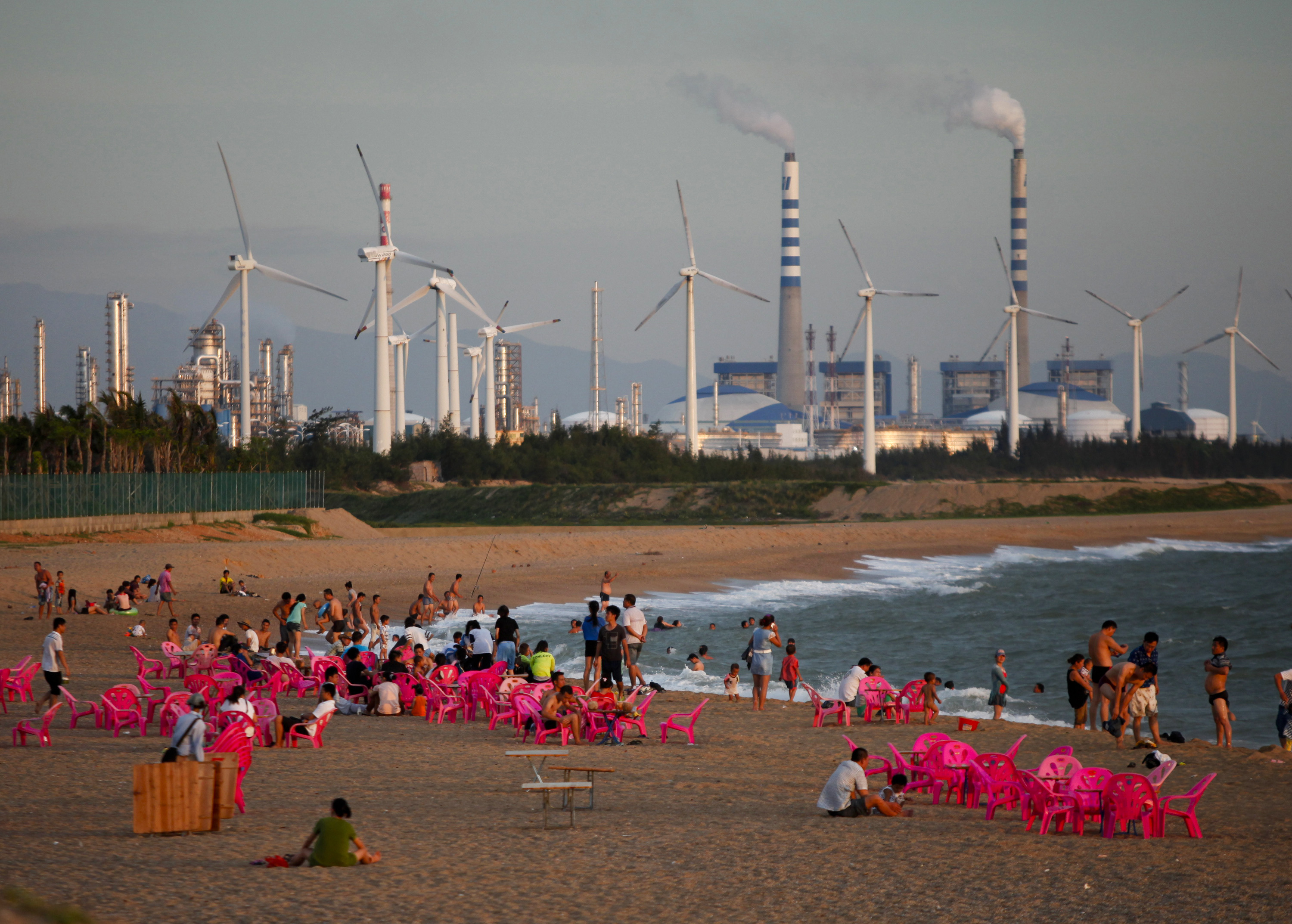 Windmills and a power plant can be seen in the distance as beachgoers watch sunset in the city of Dongfang on the western side of China's island province of Hainan